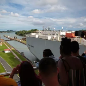 Turistas en el balcón de las esclusas de Miraflores mirando un barco pasar el Canal de Panamá