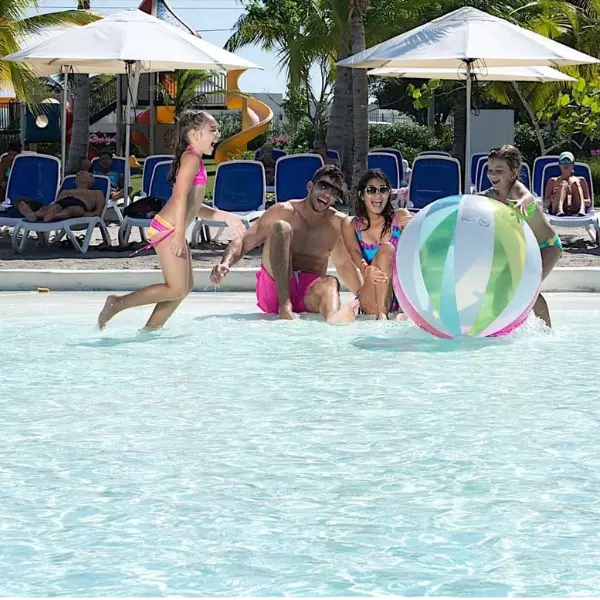 Un matrimonio y dos niños jugando alegres en la piscina de Playa Blanca Panamá con una pelota de playa